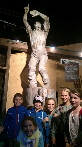Eine Gruppe Kinder vor einer geschnitzten Holzfigur.